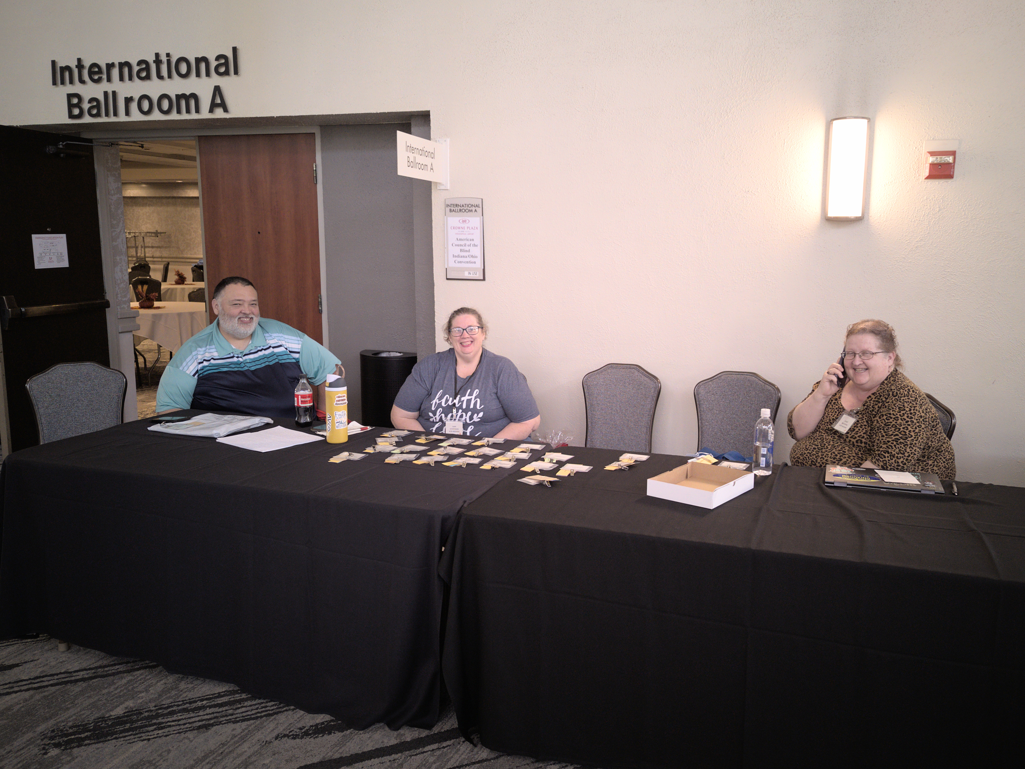 Cliff Goodman, Kari Goodman and Cindy Brooking behind registration table outside Ballroom A.