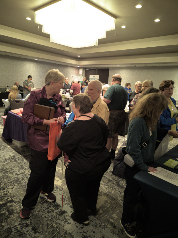 Photo taken in the exhibitors room shows Deanna Austin, Bill and Jennifer Sparks engaged in conversation. Kolby Garrison is shown at right visiting an exhibit booth. In the background within the photo Brant Adams is visiting another exhibit booth.