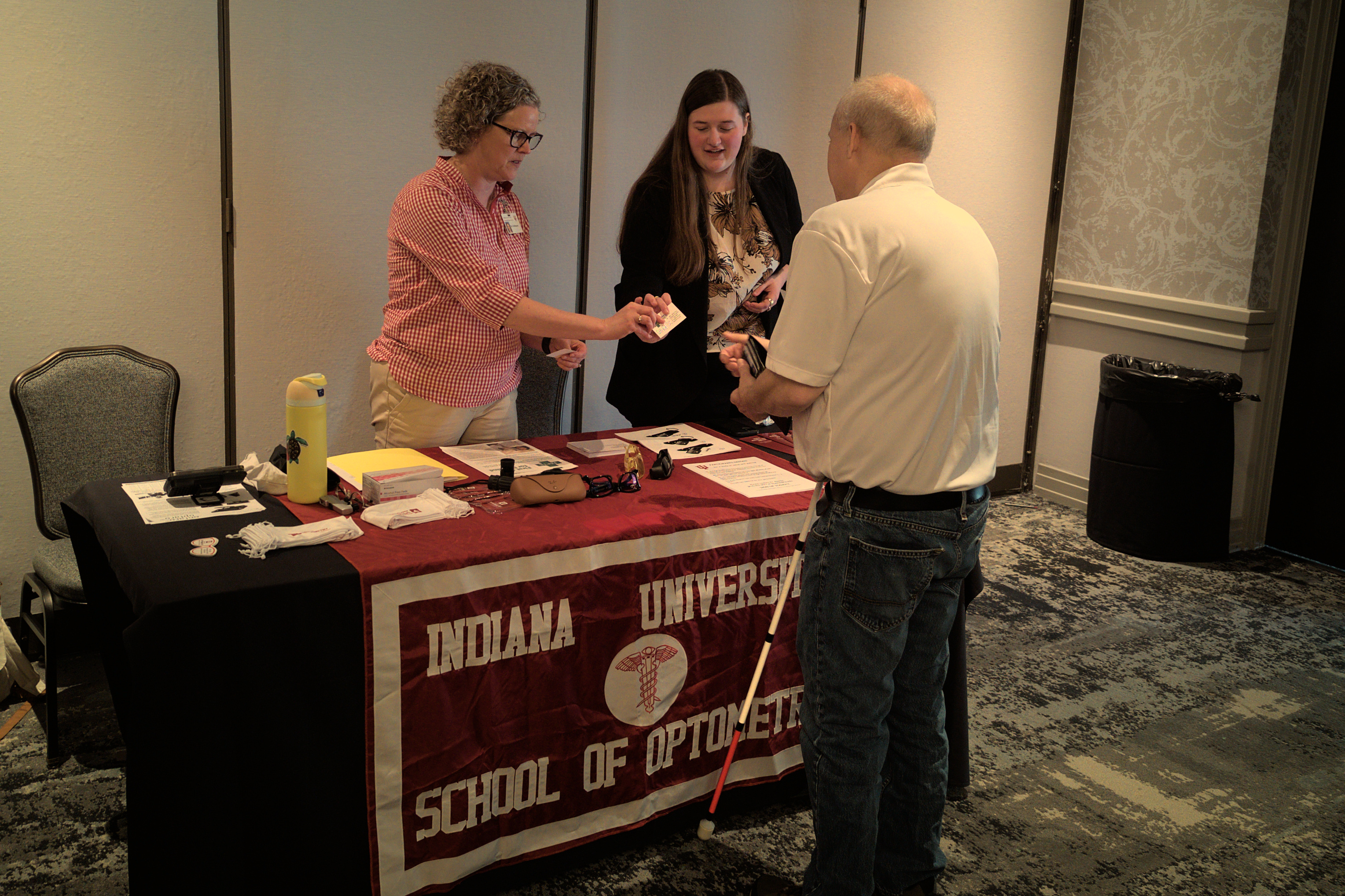 Exhibitors from the Indiana University School of Optometry interacting with a convention attendee at their booth.