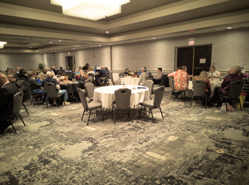 People seated at round tables talking during the banquet and auction. On the very right of the photo is a table with Cindy Brooking, Maggie and Johnathan King, Deanna Austin and Mike and three other people.